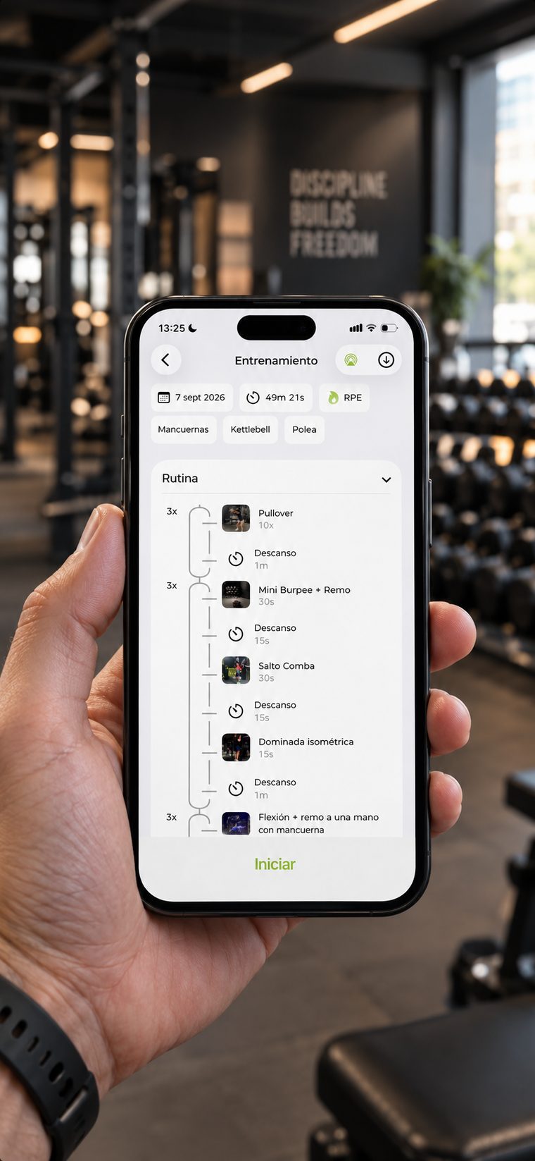 Móvil sostenido en la mano dentro de un gimnasio, mostrando la pantalla de entrenamiento de la app con la rutina del día, los tiempos de descanso y un vídeo por ejercicio.