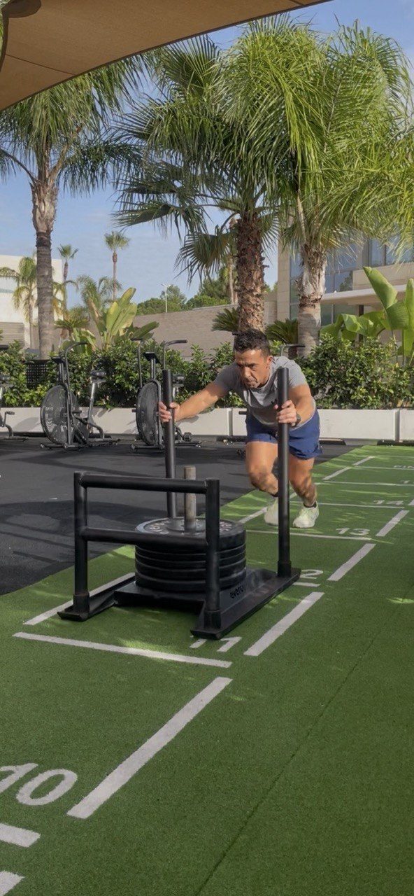 Juan Funcional empujando un trineo cargado con discos en una pista de entrenamiento al aire libre.